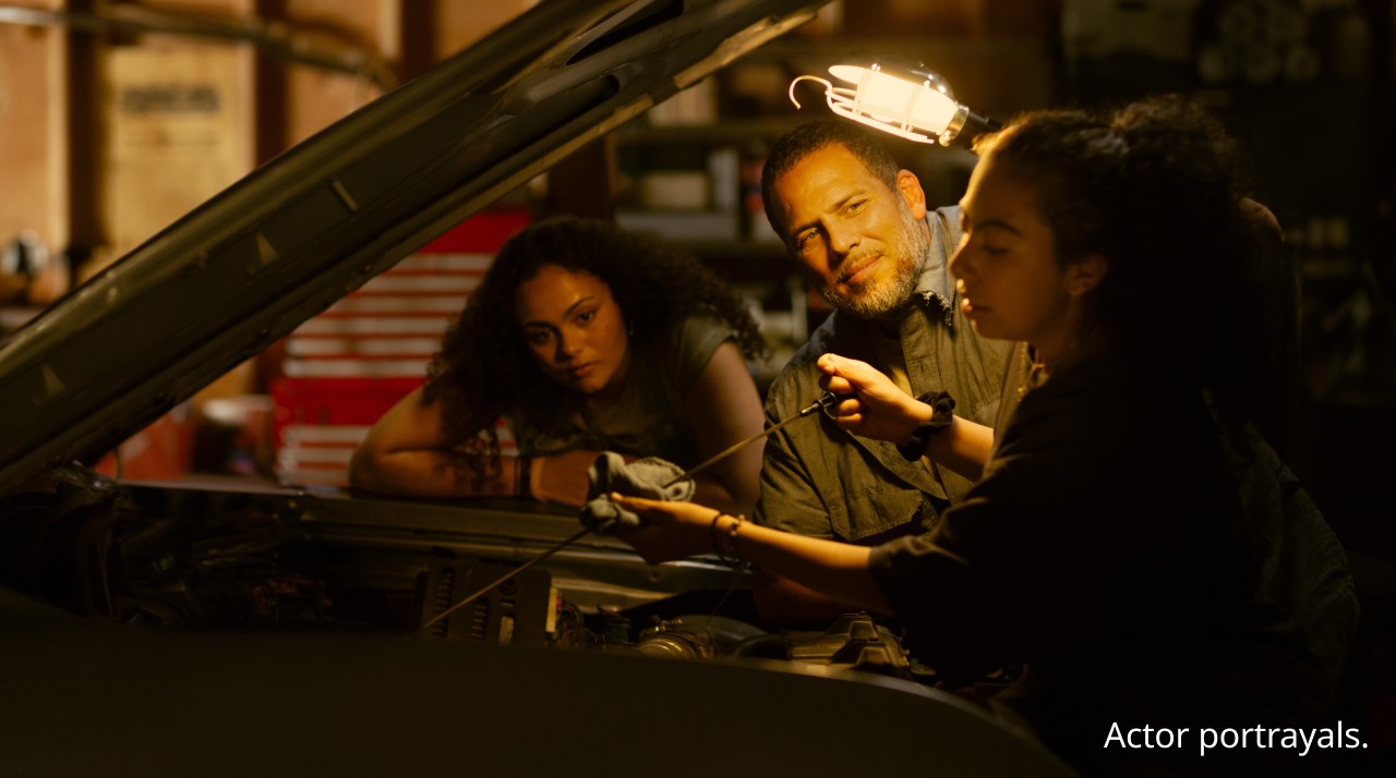 Man working on car with daughters